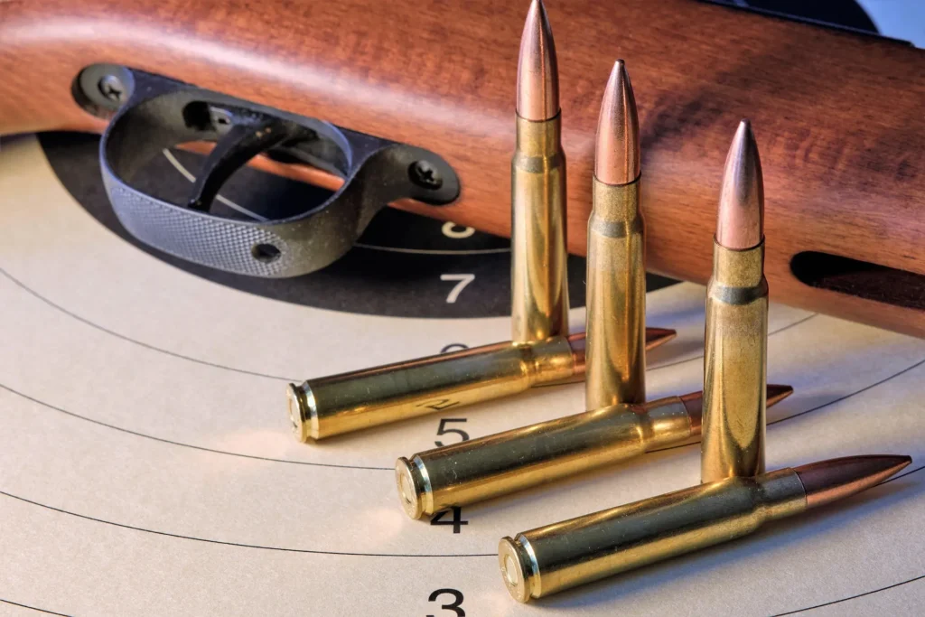 Cartouches de carabine posées sur une cible de tir sportif, à côté d'une crosse en bois